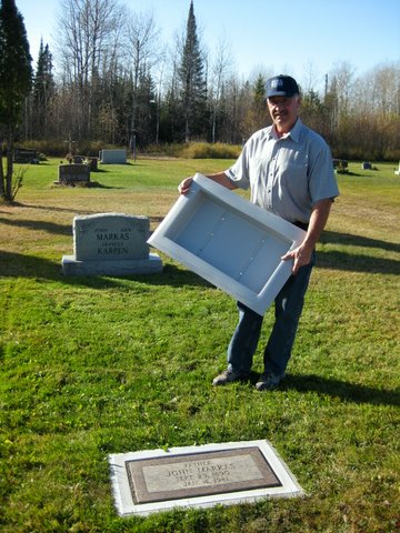John Markas holding a Grave Saver foundation beside the Markas family monument and the flat marker it protects.