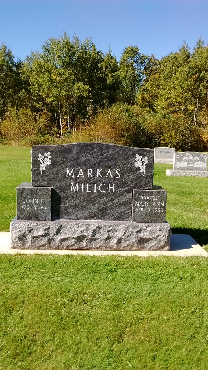 A wide black granite cremation urn monument with a companion stone at each end, set on a rough-cut granite base.