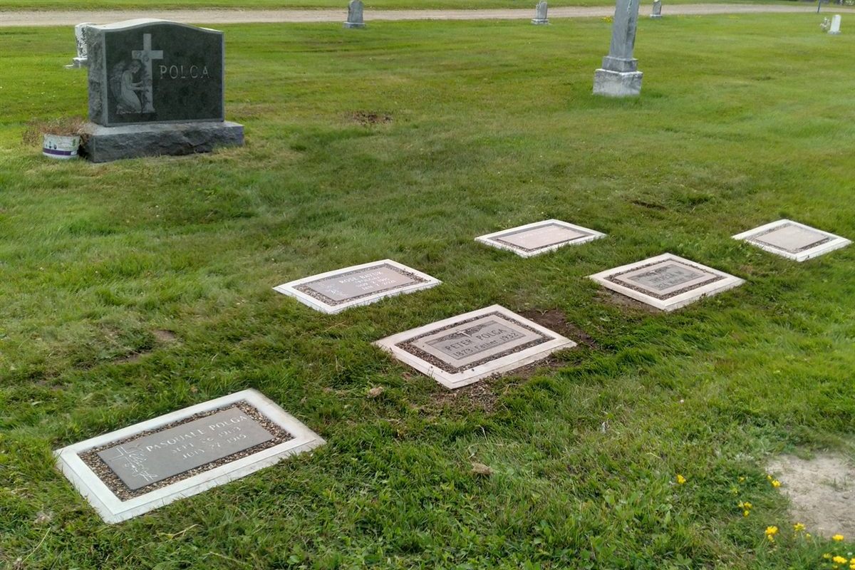 A row of flat markers set in Grave Saver frames beside an upright family headstone.