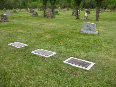 Three flat markers in Grave Saver frames laid out across a cemetery lawn.