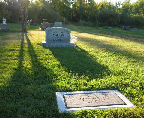 A flat marker in a Grave Saver frame in low evening light, with an upright monument behind it.