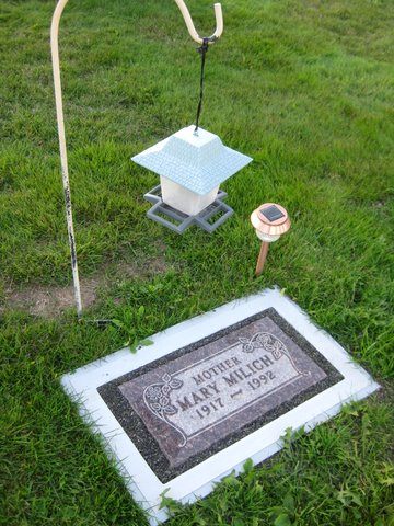 A flat granite marker framed by a white Grave Saver, with garden decorations beside it.
