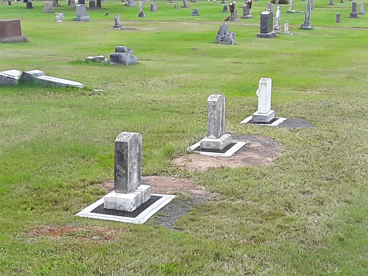 Weathered upright stones each set in a white Grave Saver frame on an older cemetery lawn.