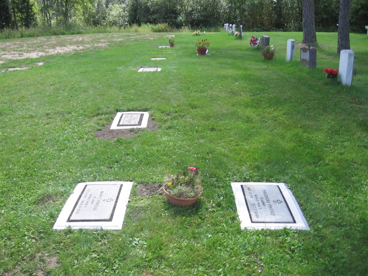 Flat markers in Grave Saver frames on a long cemetery lawn, one with a flower pot beside it.